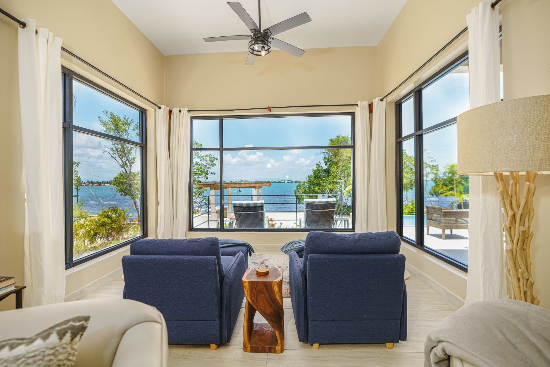 Cozy living area with two blue armchairs and large windows overlooking a tranquil waterfront view.