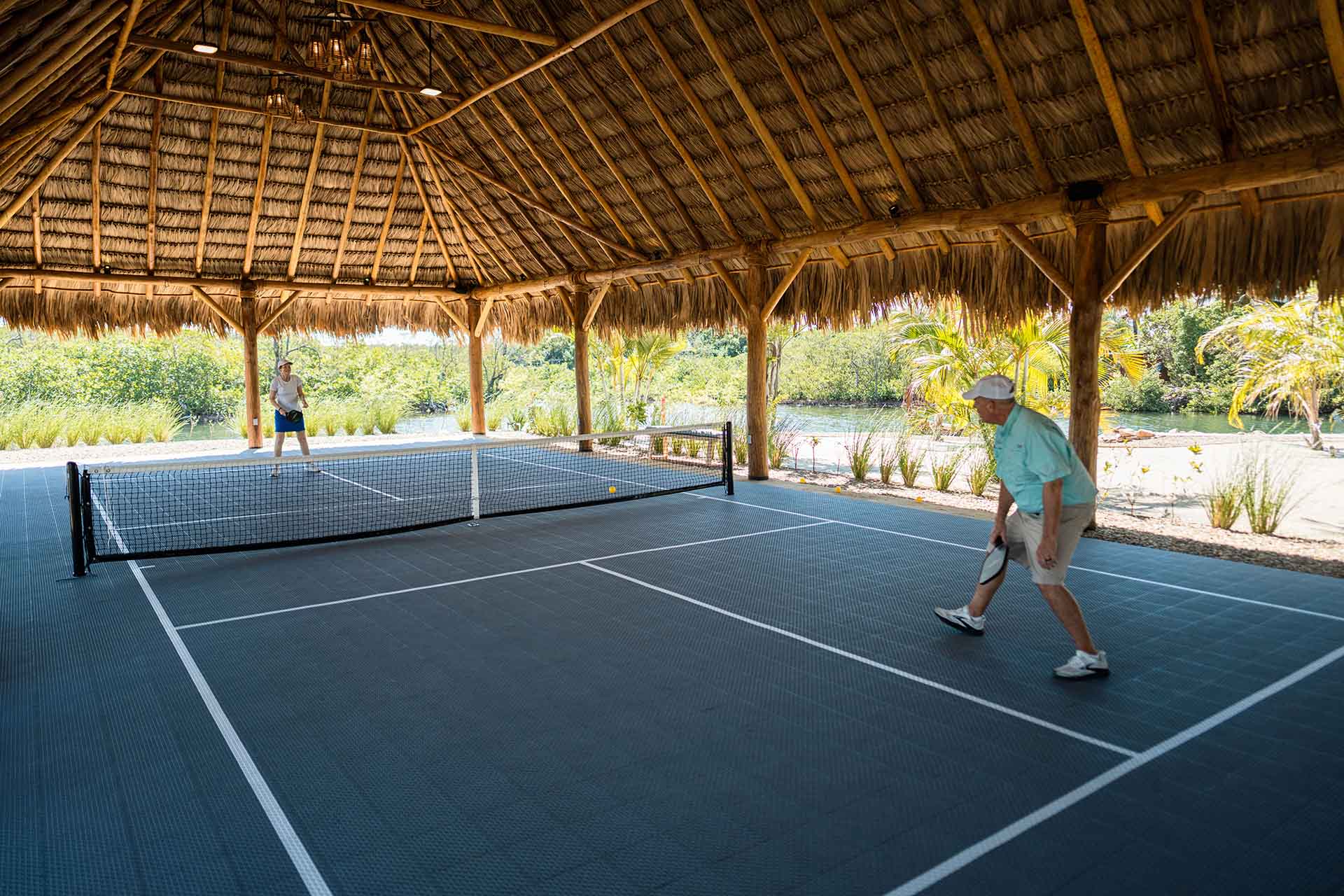 Two people playing pickleball in a shaded outdoor court.