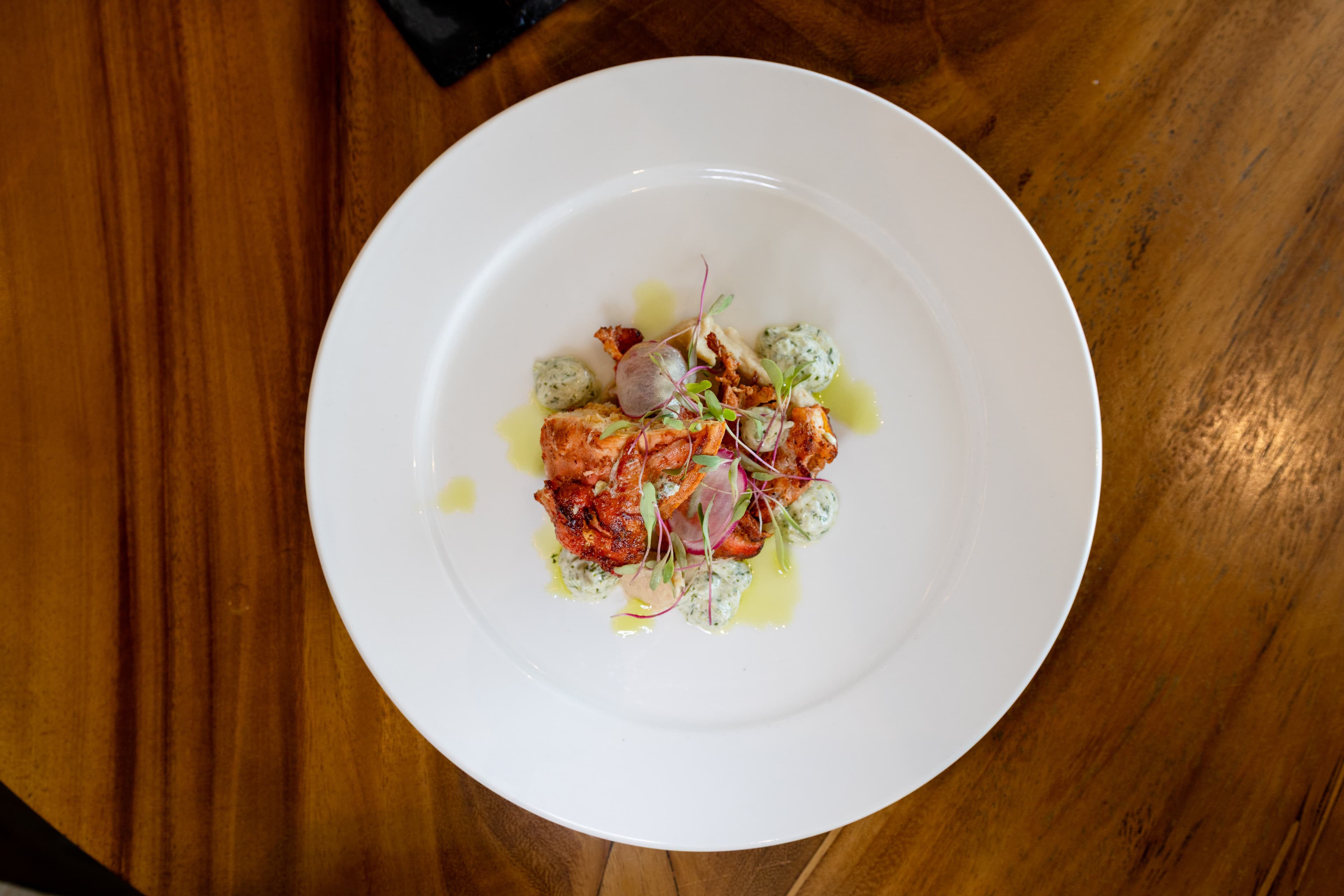 A beautifully plated dish featuring colorful garnishes and a green sauce on a white plate.