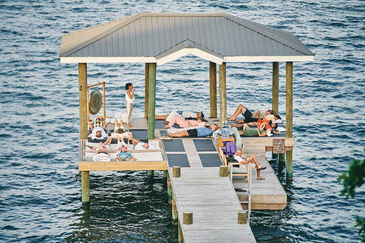 A group of people relaxes on a dock over water, with one person standing nearby.