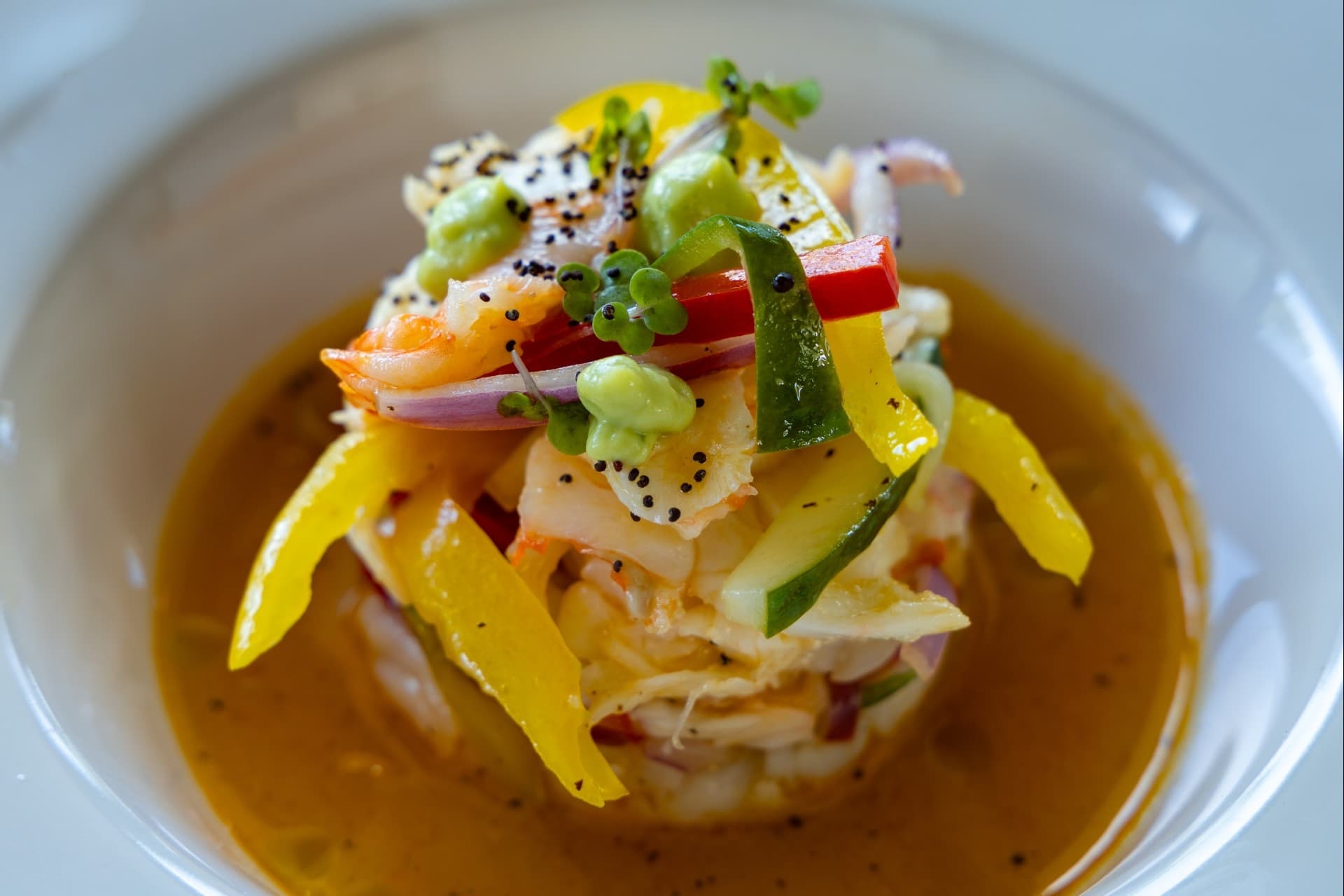 A colorful seafood dish topped with vegetables in a savory broth.