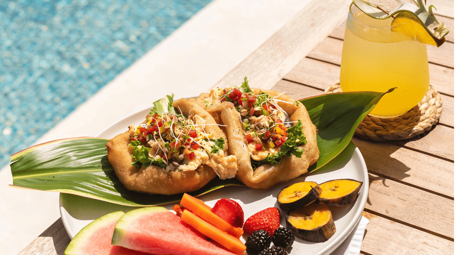 A vibrant plate of tacos accompanied by watermelon, carrots, strawberries, and a refreshing drink, set by a beautiful poolside.