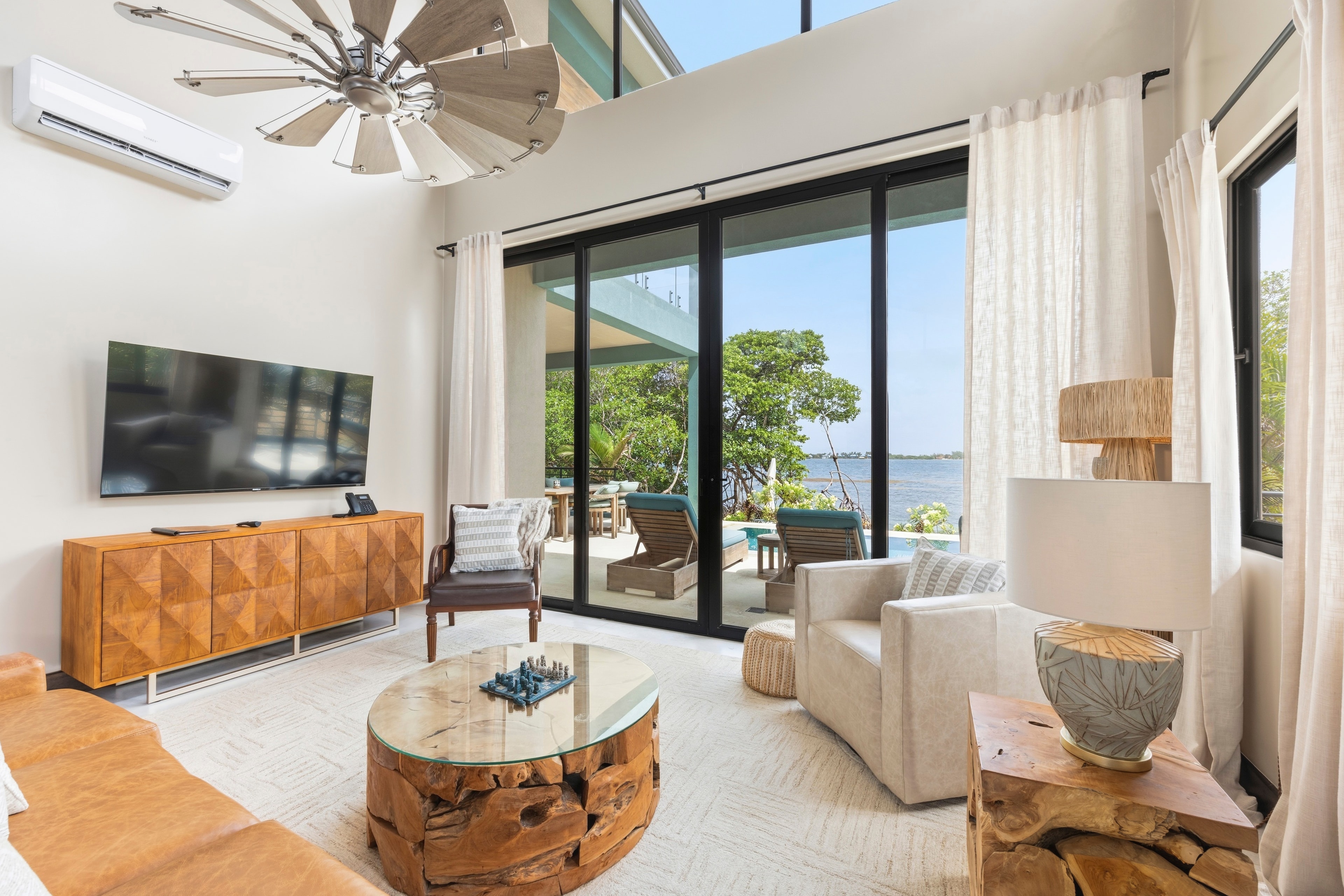A modern living room featuring large windows overlooking a patio and water, with stylish furniture and decor.