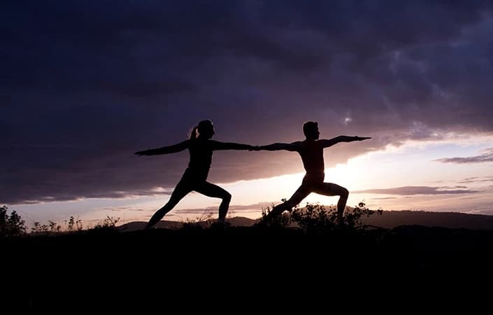 Silhouettes of two people practicing yoga poses against a dramatic sunset.