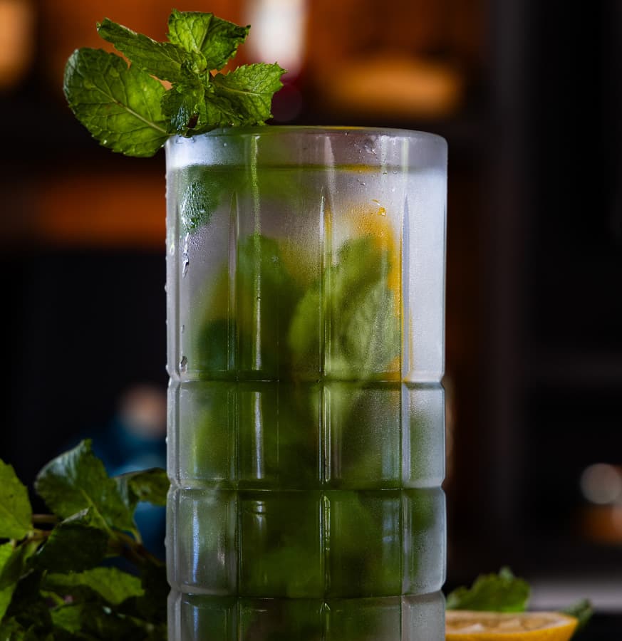 A frosted glass containing a refreshing mint cocktail with visible mint leaves and a lemon slice.