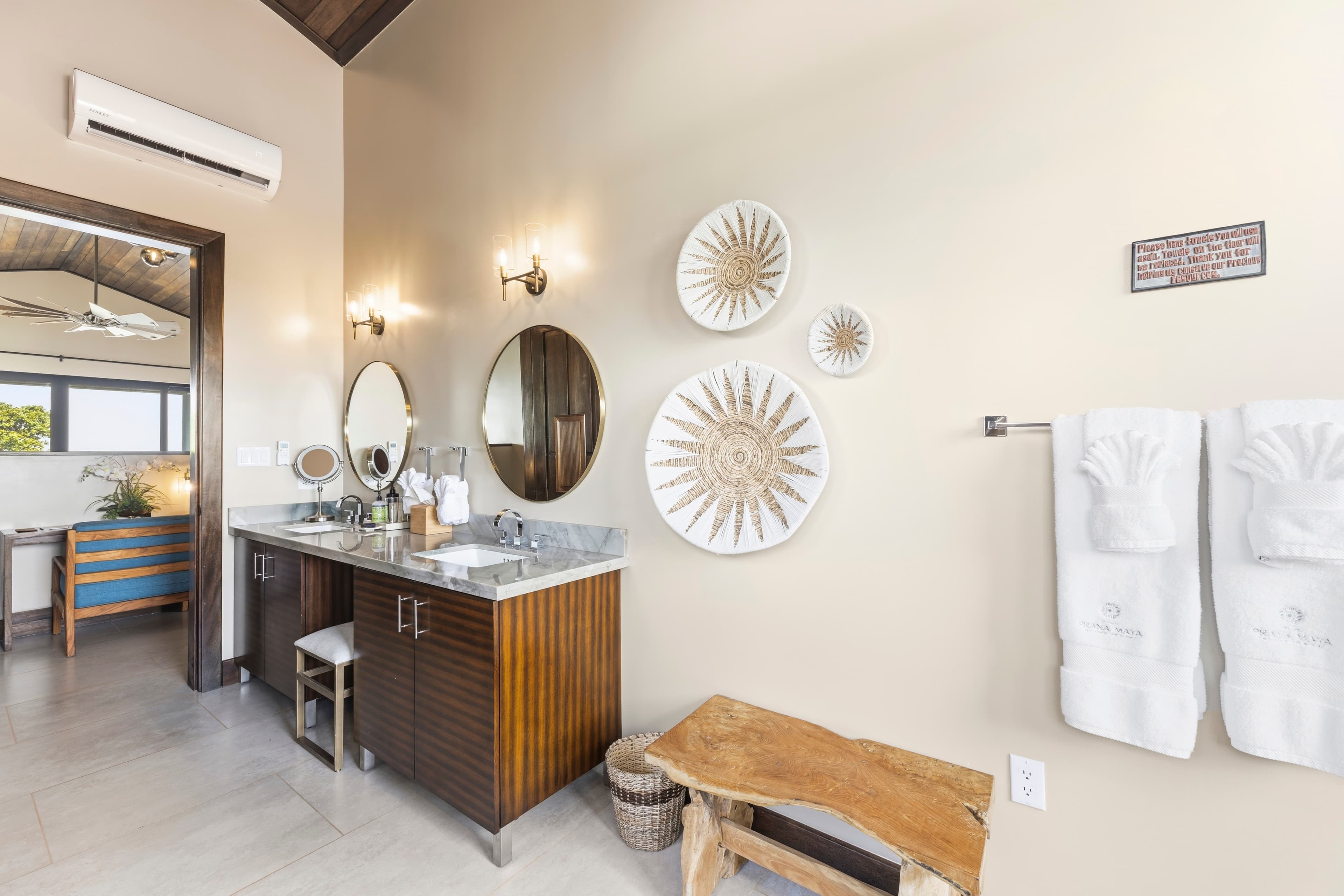 A modern bathroom featuring a double vanity, two round mirrors, decorative wall art, and white towels hanging on a rack.