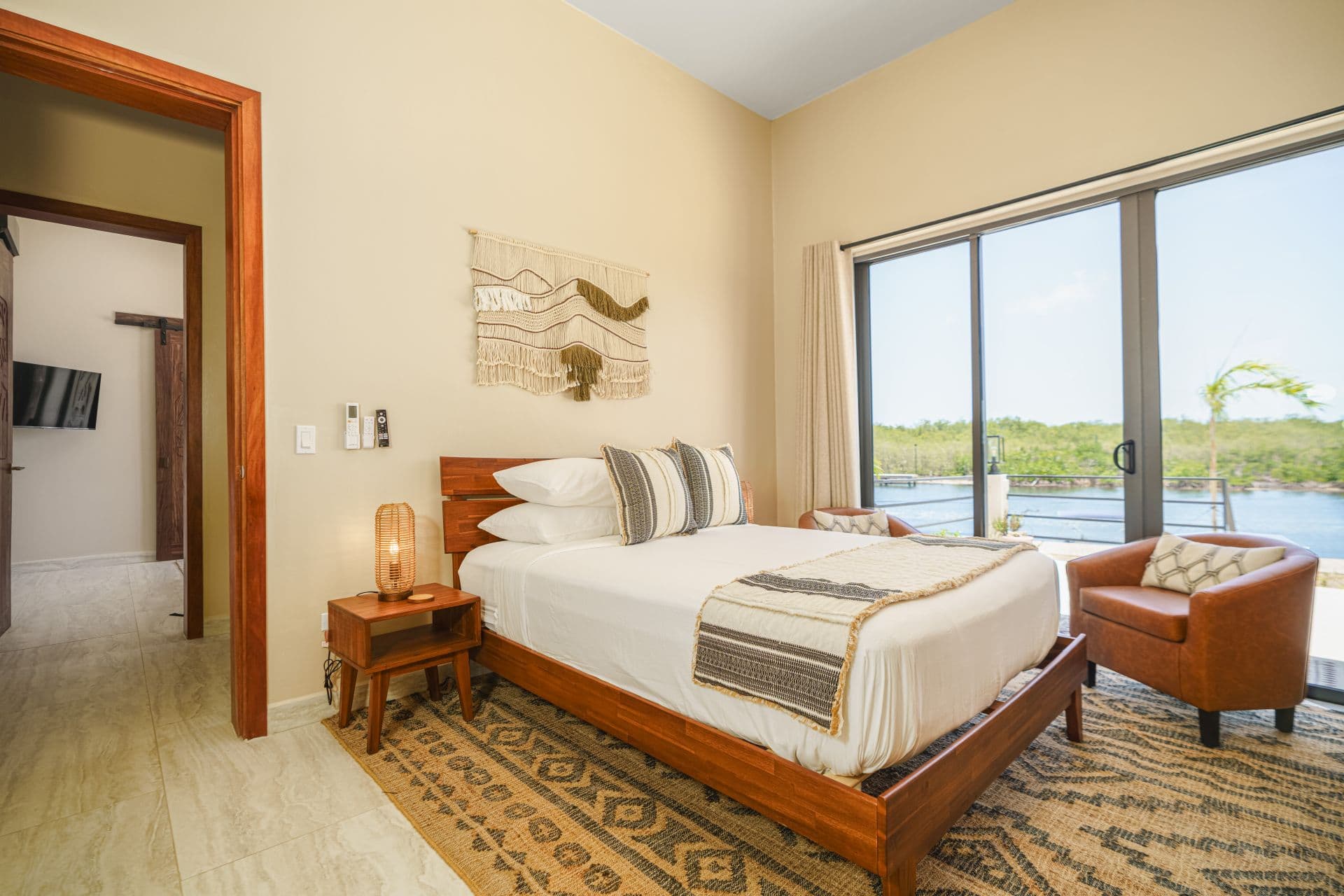 A cozy bedroom featuring a wooden bed, a chair, and large windows overlooking a scenic view.