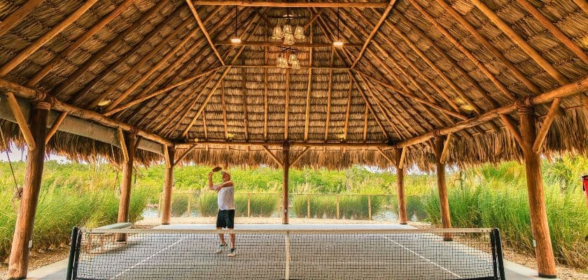 Guest plays pickleball beneath the thatched palapa covering Prana Maya Island Resorts pickleball court.
