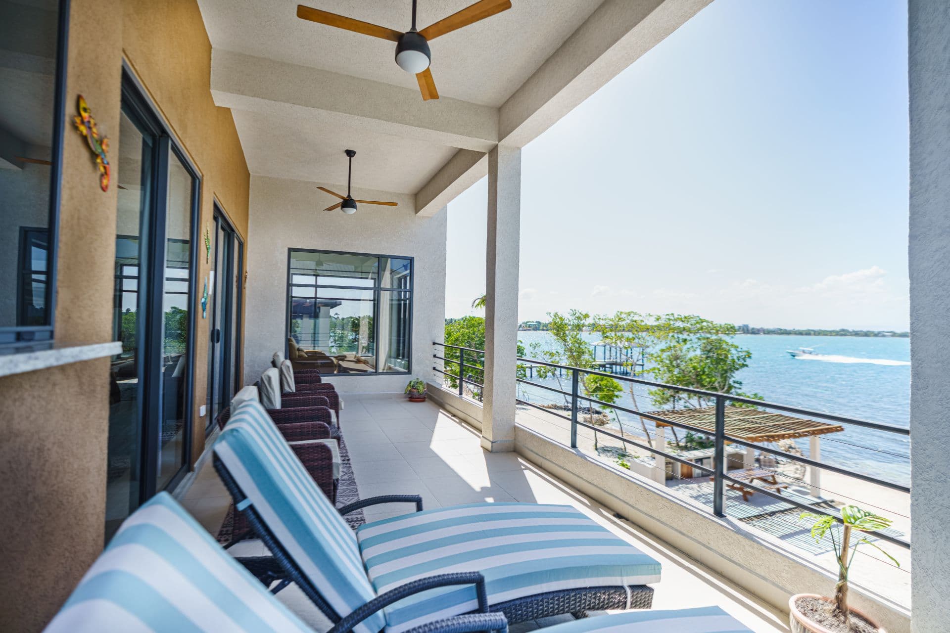 A bright outdoor seating area with striped lounge chairs overlooks a tranquil body of water.