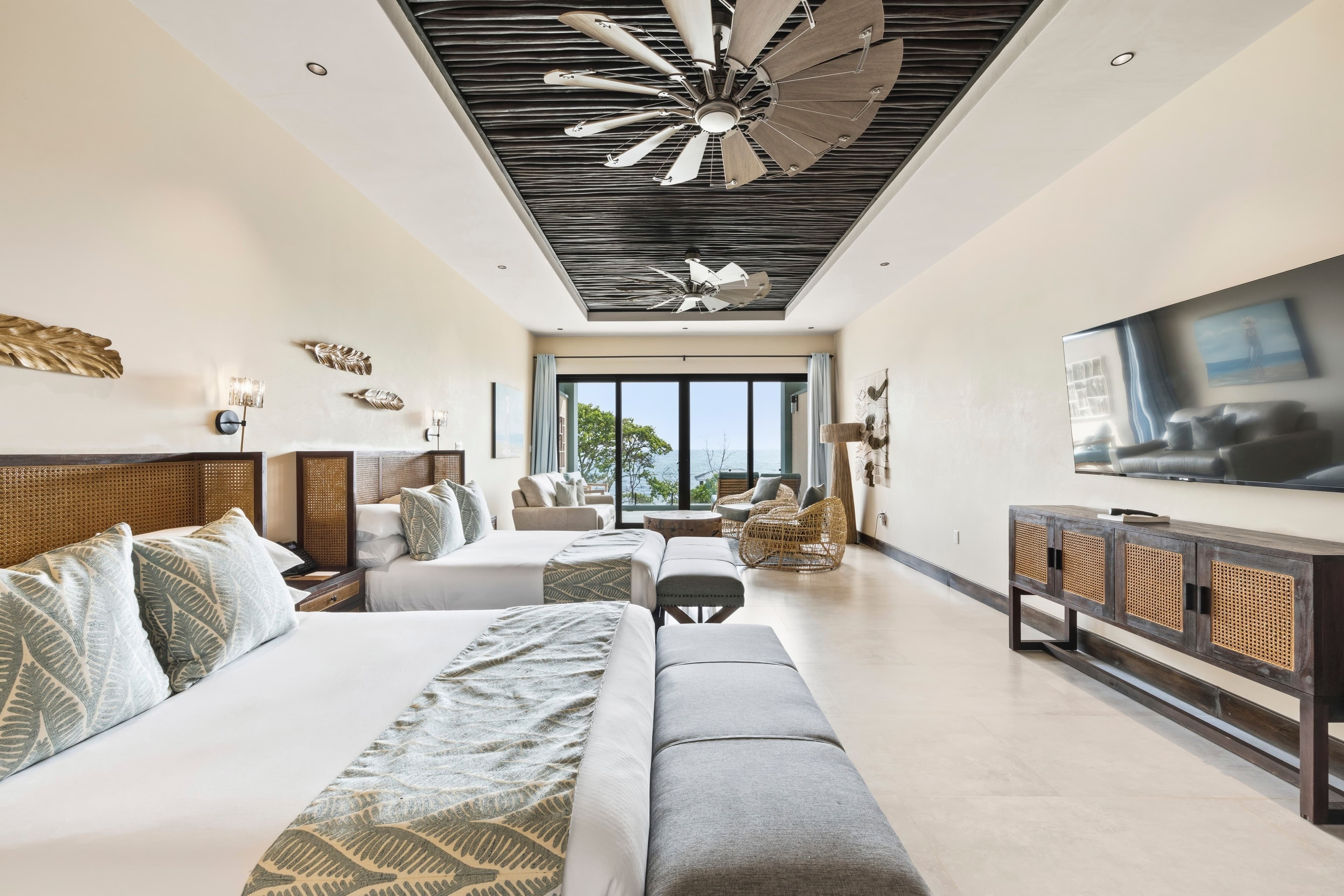 A spacious hotel room featuring two beds, natural decor, and large windows with a sea view.