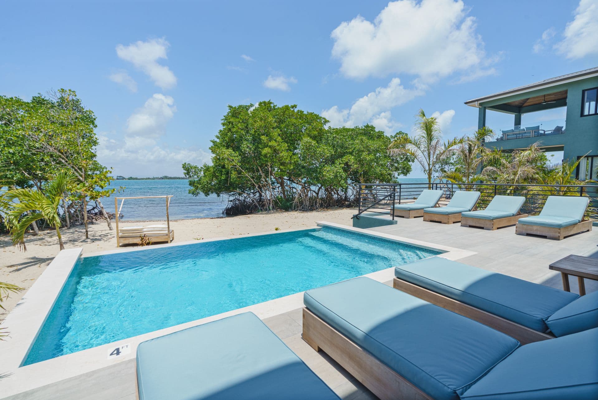 A modern pool area with lounge chairs overlooks a serene coastal landscape and mangroves.