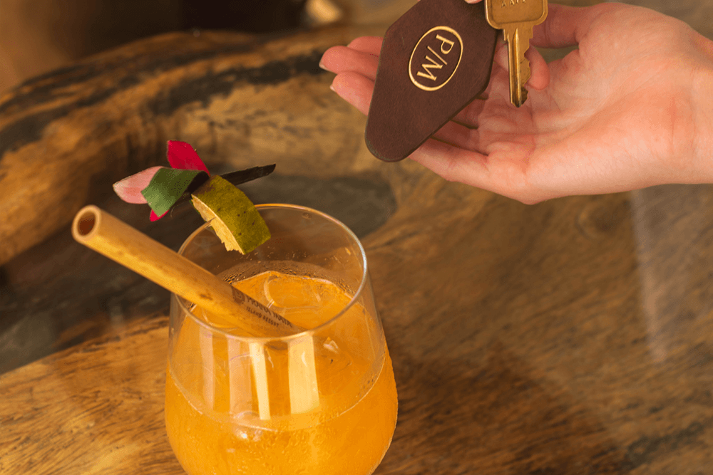 A hand holds a key card above a cocktail garnished with a bamboo straw and lime.