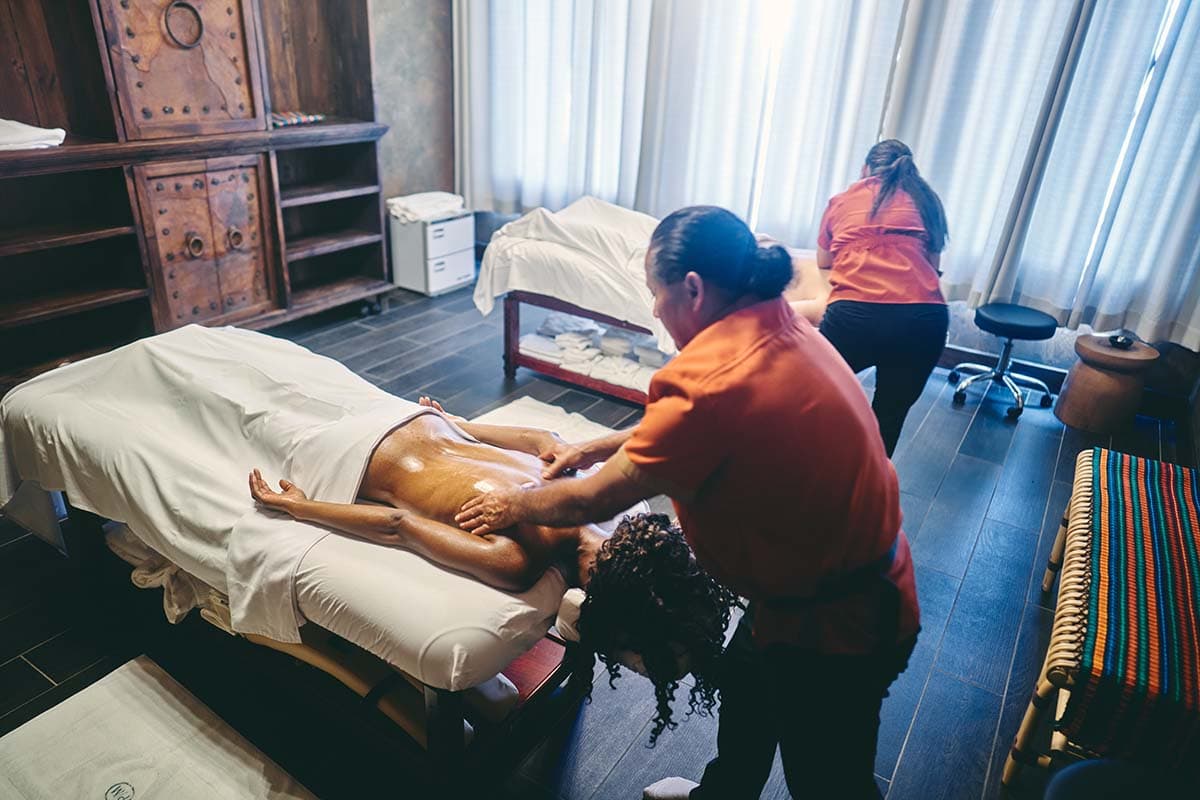 Two therapists are giving massages to clients in a serene spa setting.