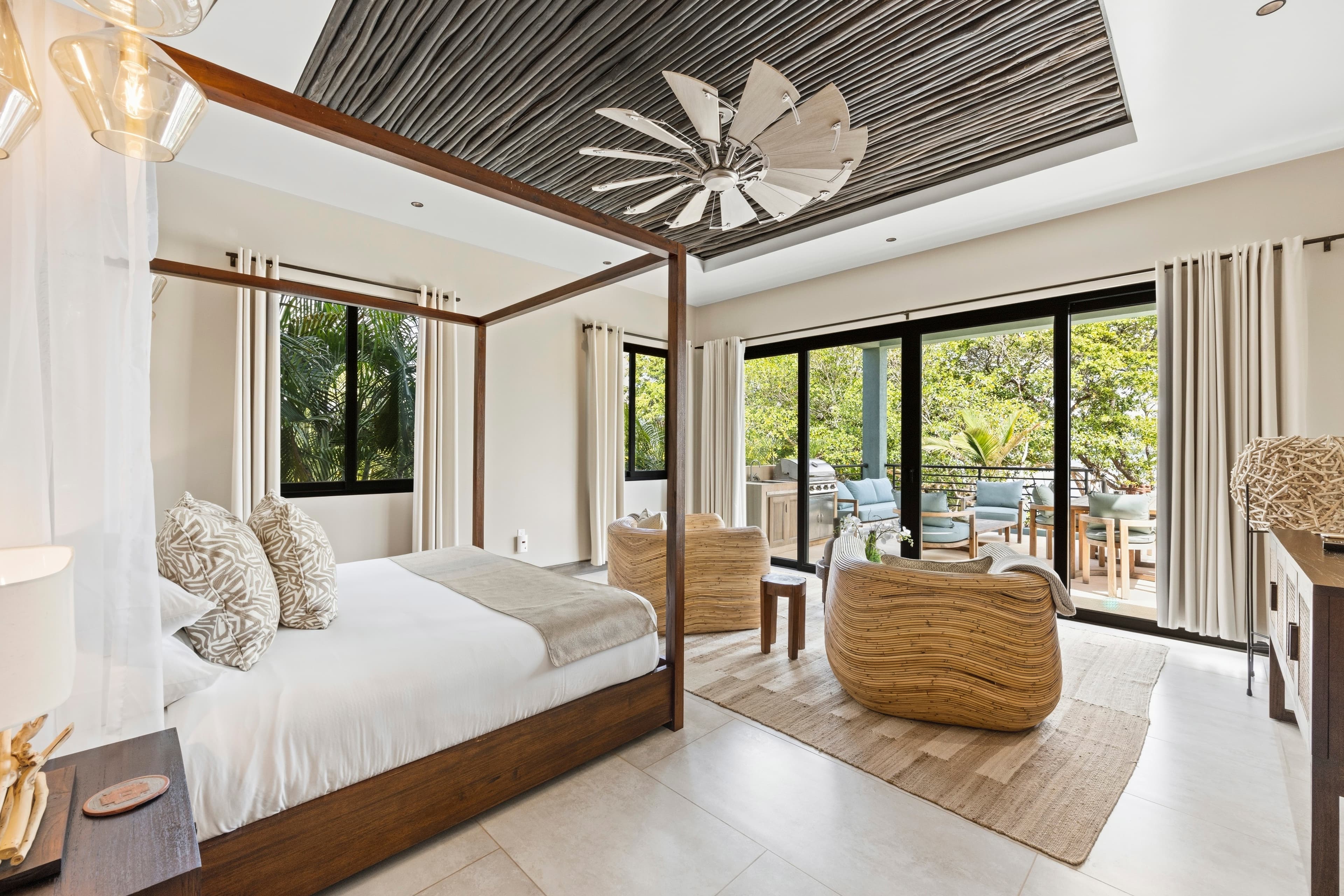 A stylish bedroom featuring a four-poster bed, two armchairs, and large windows with views of greenery.