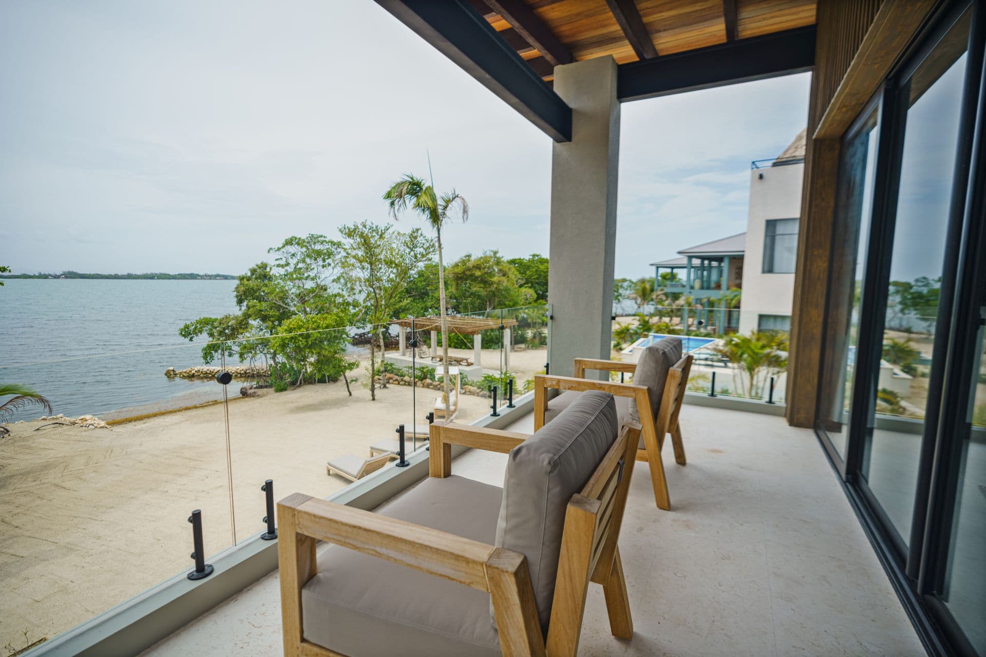 A spacious balcony with two wooden chairs overlooks a serene lake surrounded by greenery.