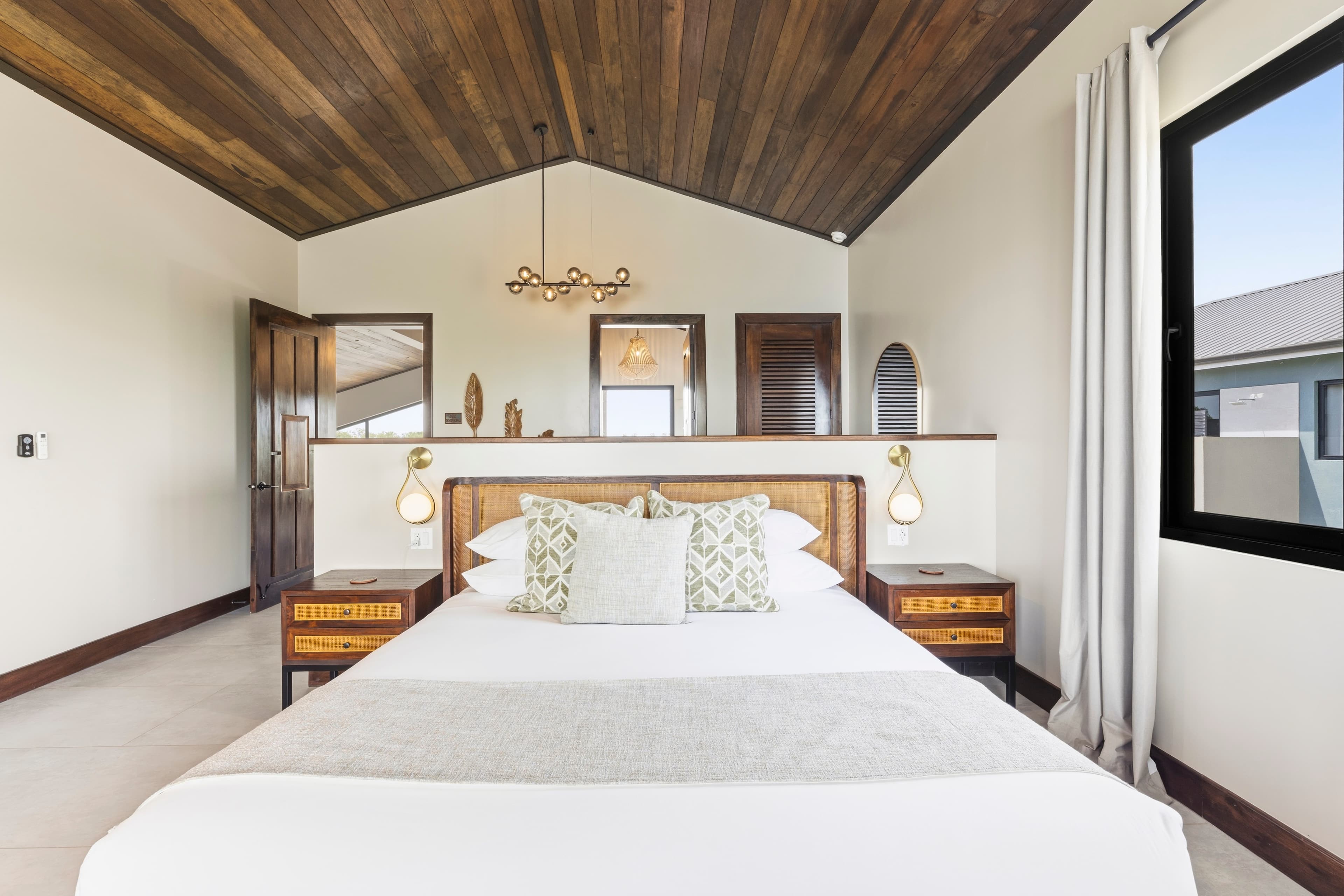A modern bedroom featuring a king-sized bed, wooden ceiling, and large windows.