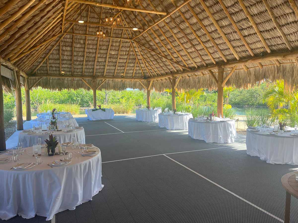 An outdoor event space with tables elegantly set under a thatched roof.