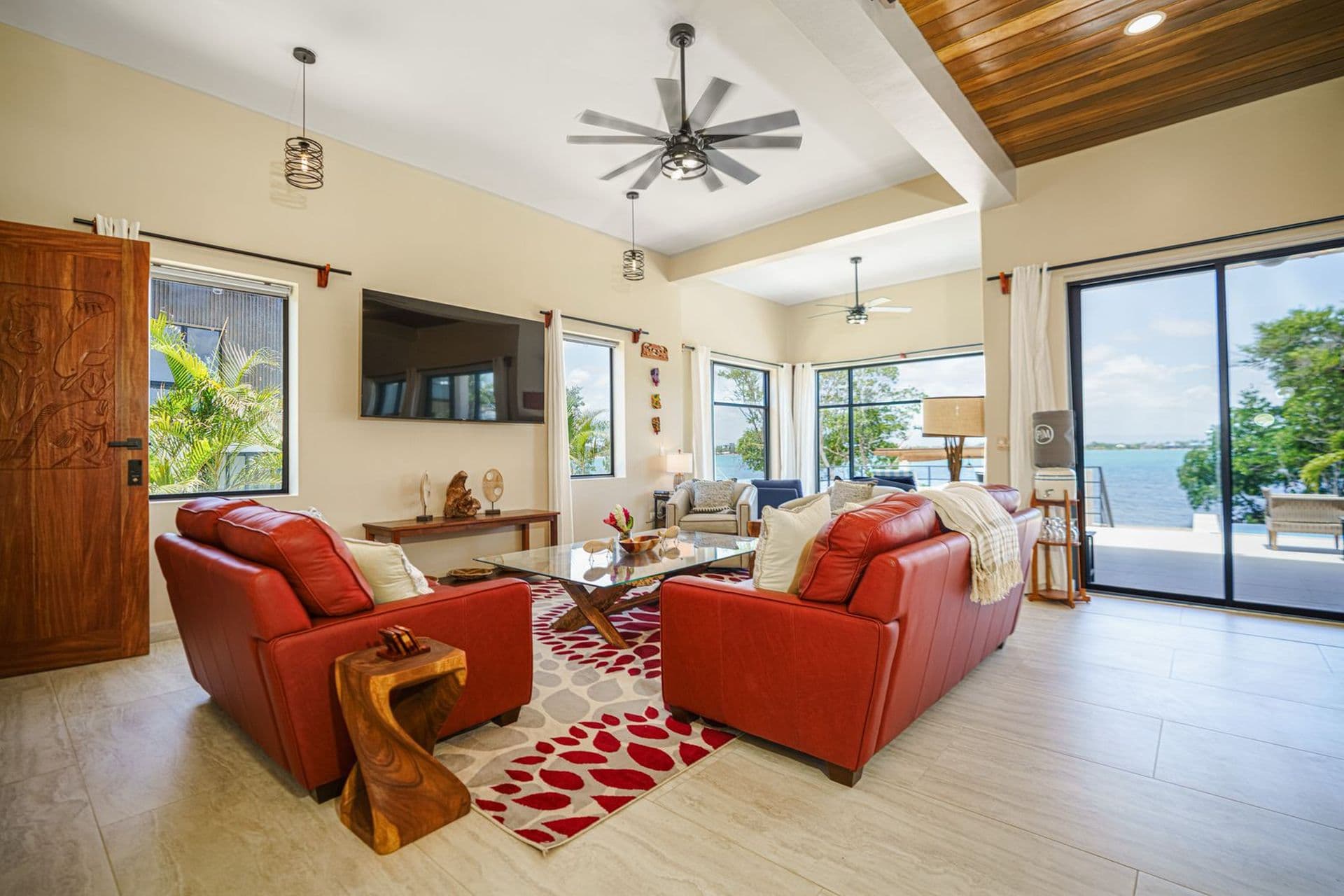 Modern living room with red sofas, a decorative rug, and large windows overlooking a scenic view.