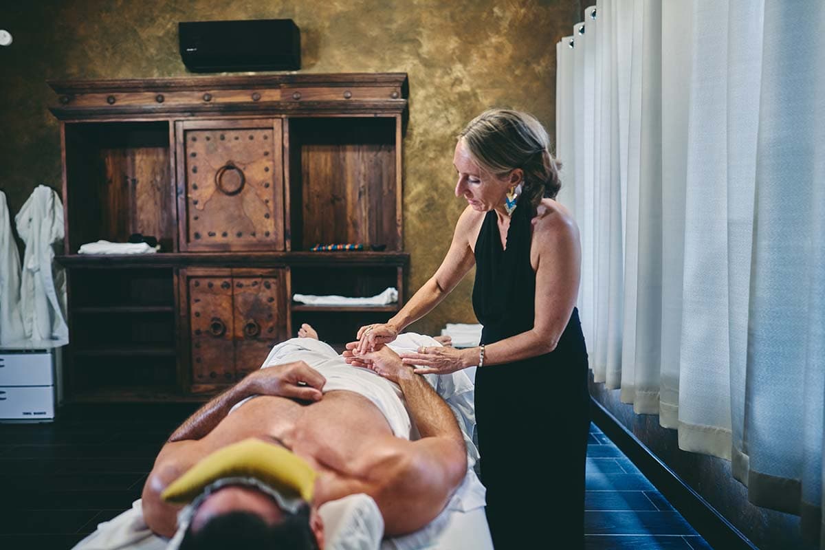 A woman gives a massage to a man lying on a treatment table in a serene spa setting.