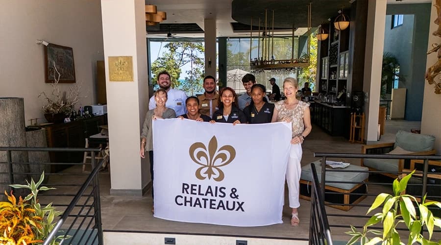 A group of staff members standing in a hospitality setting, proudly holding a flag for Relais & Châteaux.