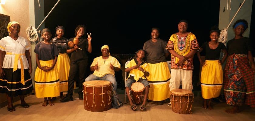 A group of Garifuna drummers and dancers in yellow and black outfits posing together at Prana Maya Island Resort.
