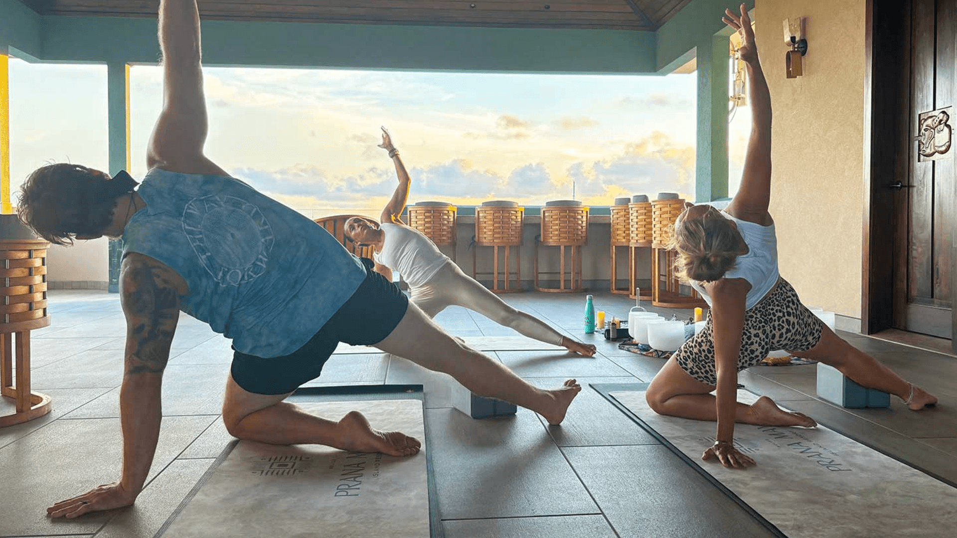 Three people practicing yoga on mats in a serene open space with sunset views.