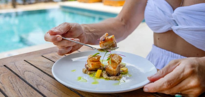 Guest eating pork belly with a citrus garnish poolside at Prana Maya Island Resort in Belize.