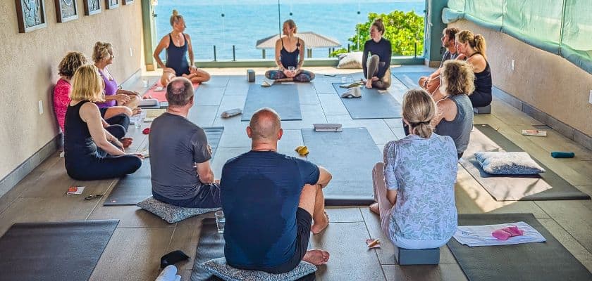 A group of people participating in a yoga class with ocean views in an open-air studio.