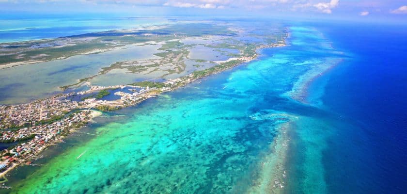 Aerial view of the Belize Barrier Reef with vibrant turquoise water, coral formations, and the coastline stretching into the distance.