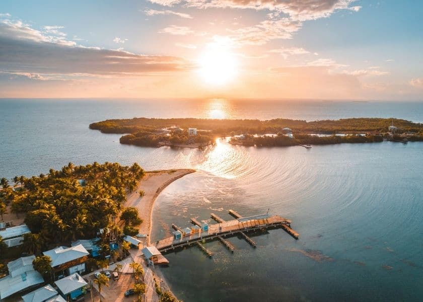 Aerial view of Placencia, Belize, at sunset with a peaceful bay, docks, palm trees, and the Caribbean Sea