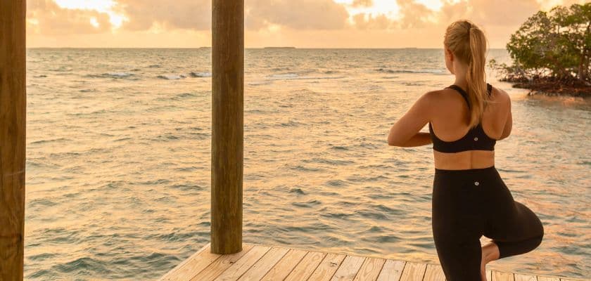 Person practicing yoga in tree pose on a dock overlooking the Caribbean Sea at sunrise.